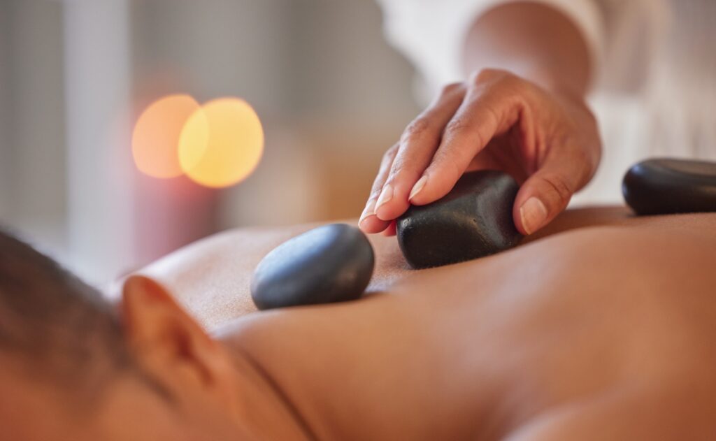 Hånd placerer sten på ryggen af patient, der modtager hot stone massage